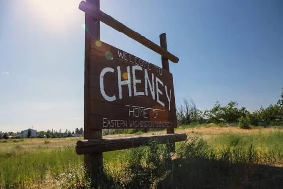 Wooden Welcome to Cheney sign, Home of Eastern Washington University, beside a grassy field in Cheney, WA