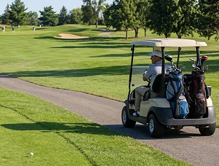 Golfer in a cart on a paved asphalt golf cart path beside a fairway, an example of golf cart path paving in Spokane, WA