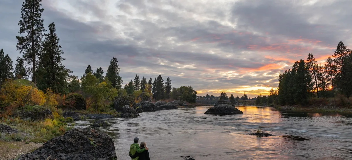 Sunset over the Spokane River with basalt boulders and tall pine trees in the Spokane Valley, WA